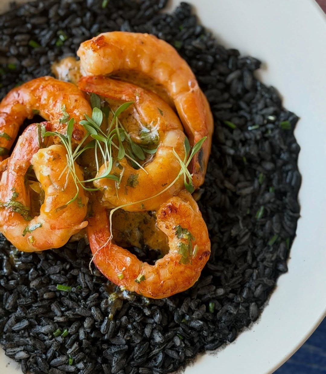 Arroz escuro com camarões grandes e rebentos verdes num prato branco
